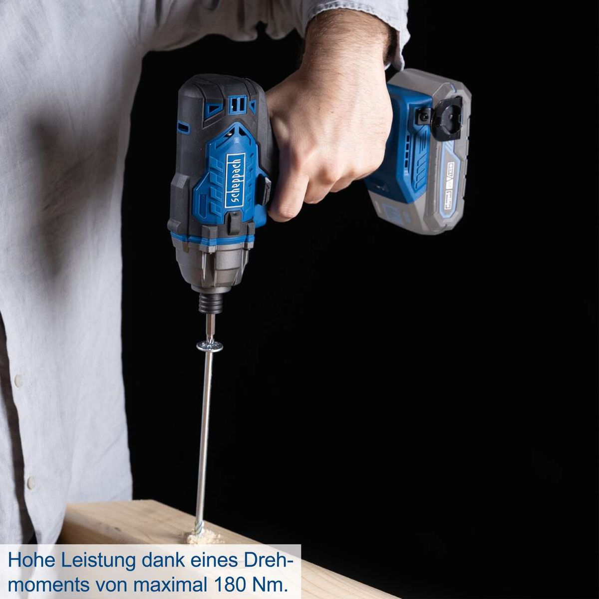 Osoba trzyma niebiesko-czarną wiertarkę. Wkręca się śrubę w drewnianą deskę.