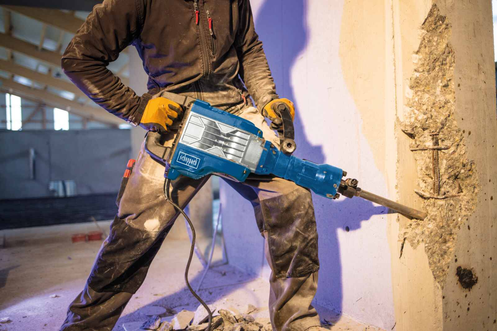 Persona usa martello demolitore blu e nero per rompere un muro di cemento.