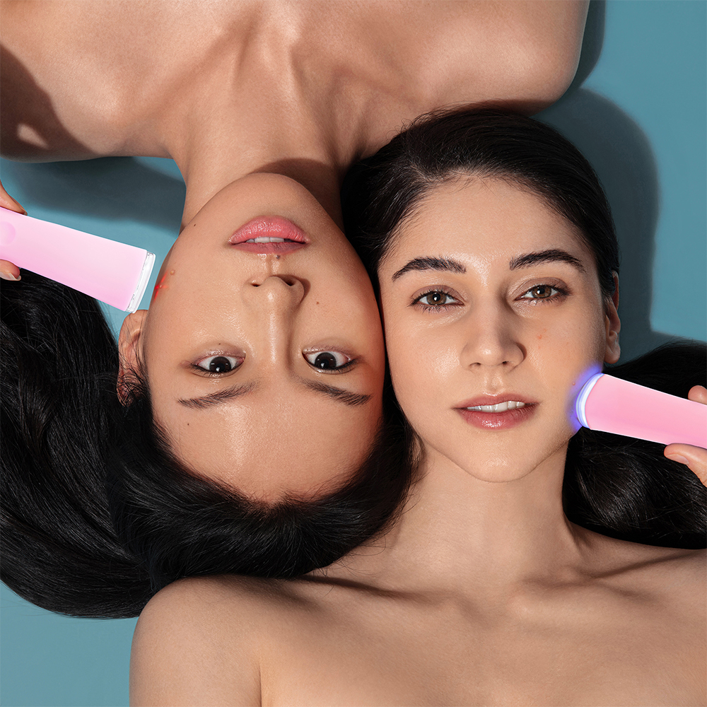 Two women with pink skincare tools. One with red light, one with blue, on a blue background.