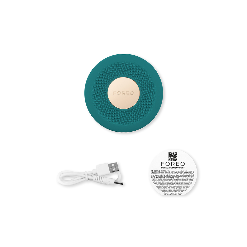 Een turquoise Foreo-apparaat en accessoires op een wit oppervlak. Een oplaadkabel en een supportkaart zijn ook zichtbaar.