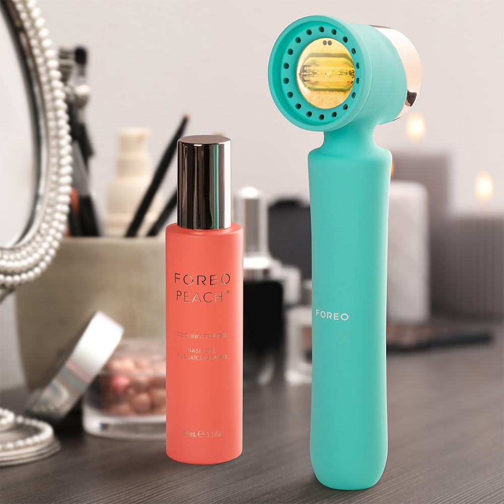 Un appareil facial et une bouteille d'huile de soin sont sur une coiffeuse. Miroir et bougies en arrière-plan.