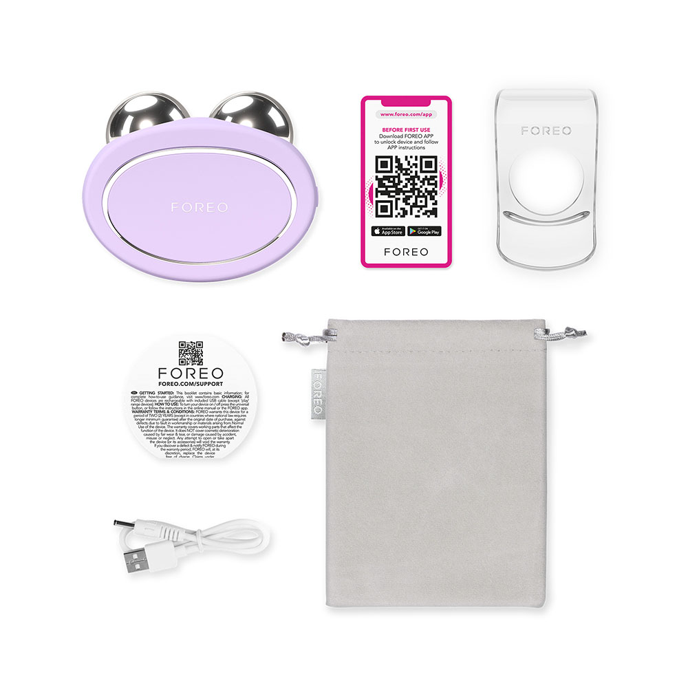 Un plat de l'appareil Foreo, câble de charge, téléphone et autres accessoires. Pochette grise et la boîte Foreo est présente.