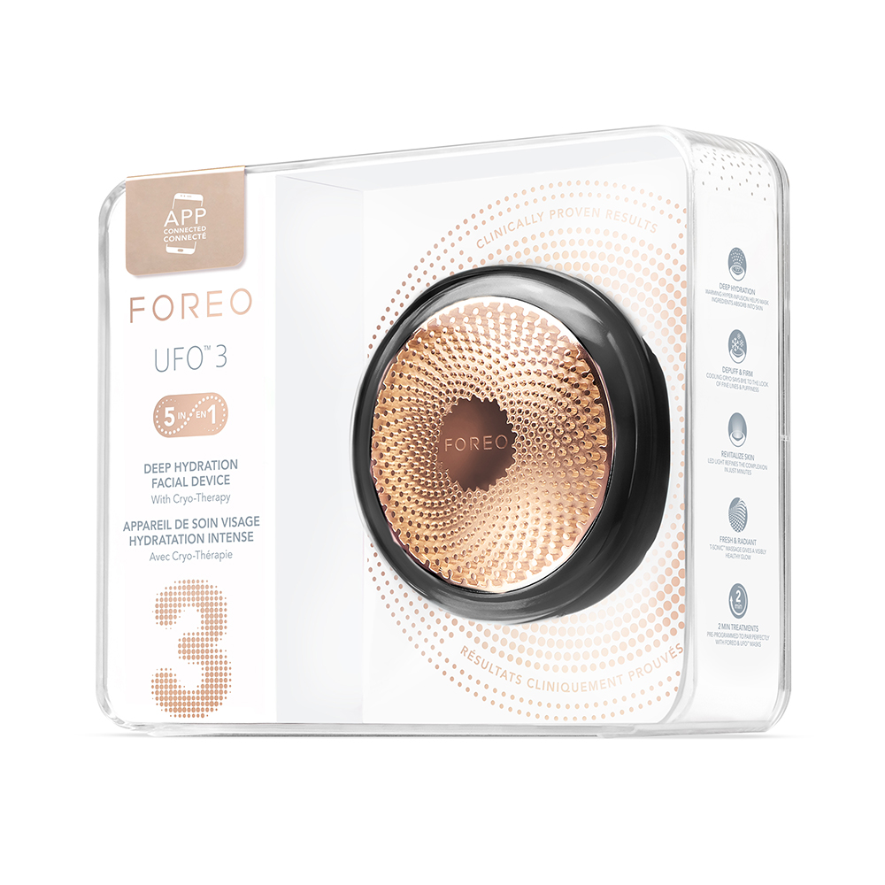 Transparante doos met een Foreo UFO 3-apparaat erin. Het apparaat is zwart en goud, met een brochure aan de zijkant.