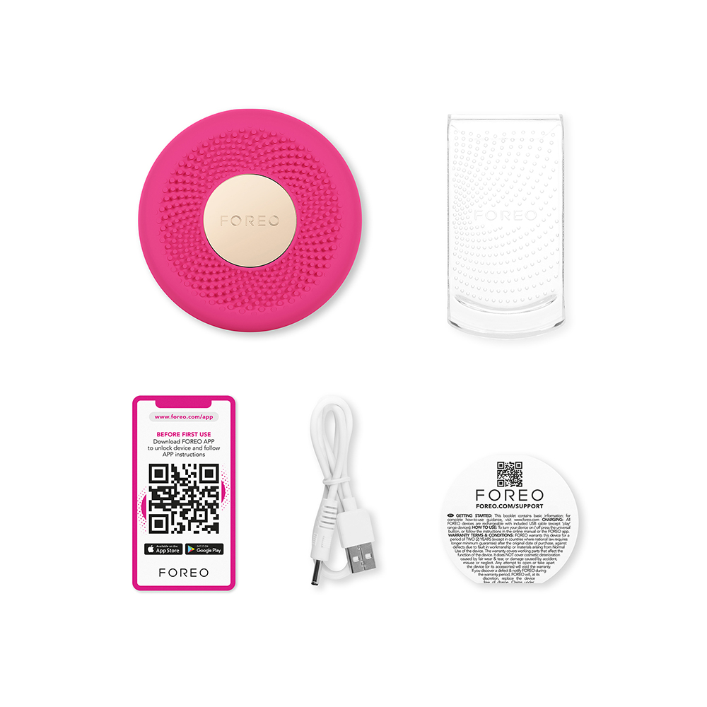 Foreo-apparaat, roze met een goudkleurig centrum. Er is een oplaadstandaard, QR-code en een handleiding. Witte achtergrond.