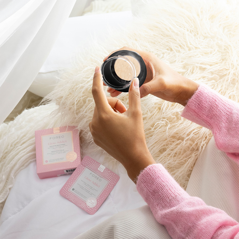 Vrouw die een Foreo-product vasthoudt, naast een roze doos en kaart.