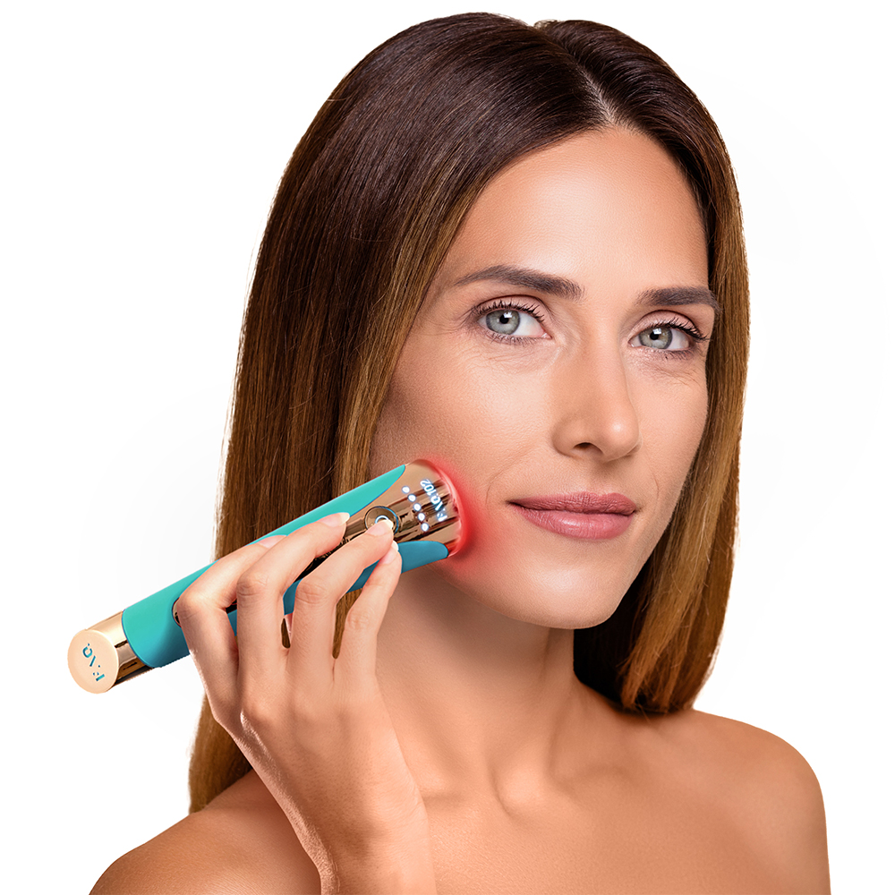 Woman holding a teal and gold Foreo device near her face. She is in a white background.