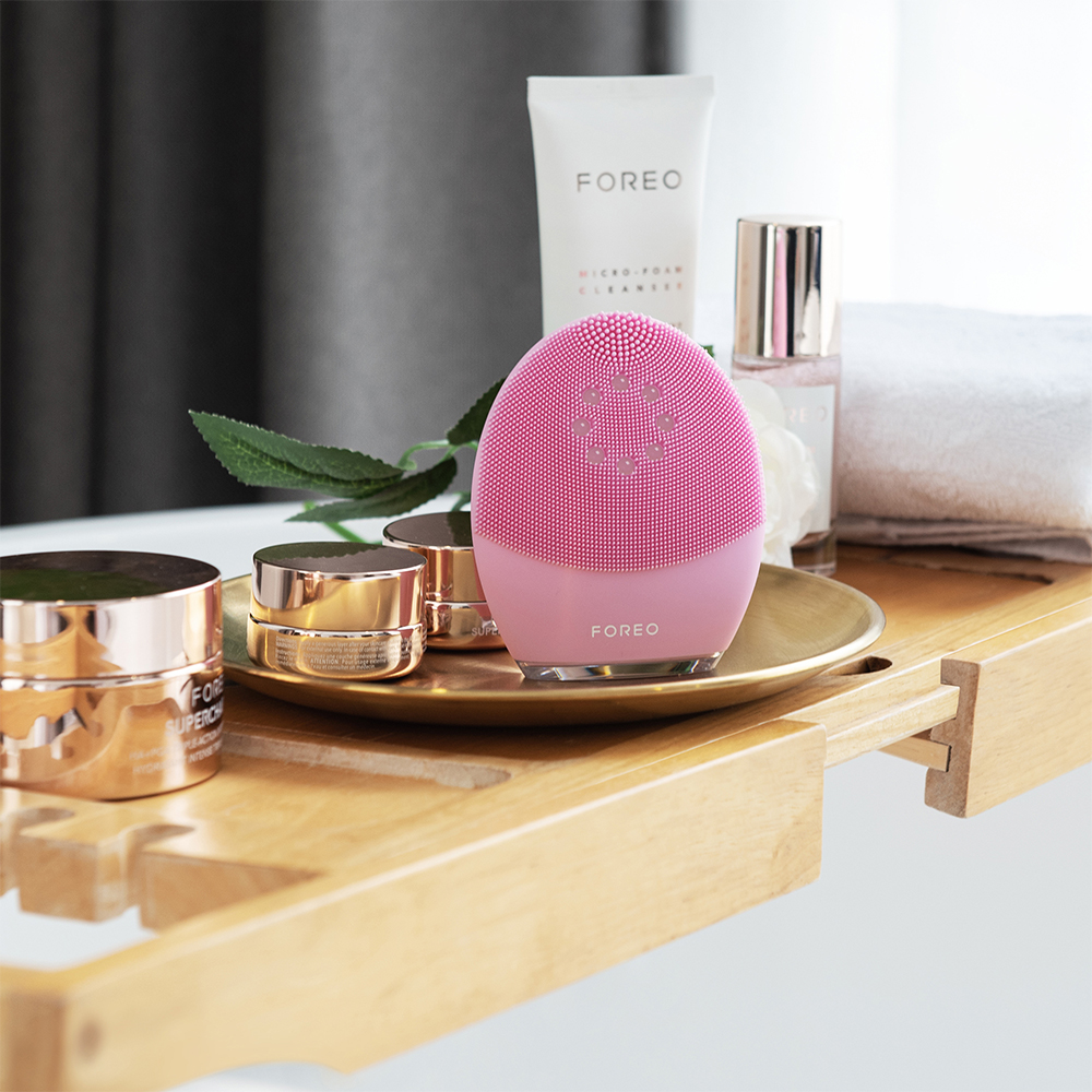 Pembe Foreo cihazı, banyo ortamında diğer cilt bakım ürünleriyle birlikte bir tepside.