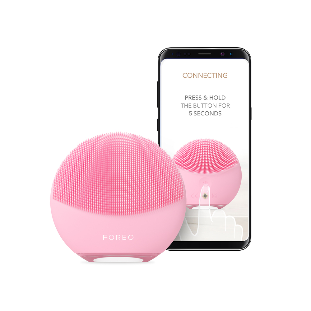 Pembe yüz temizleme cihazı, talimatları gösteren bir akıllı telefon ekranının yanında. Beyaz arka plan.