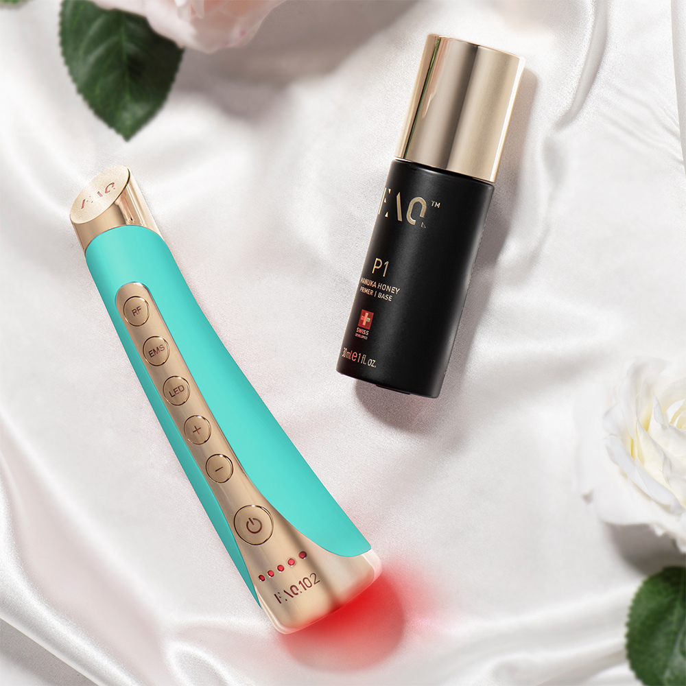 Teal device and serum bottle on white silk. Gold accents on device. White background.