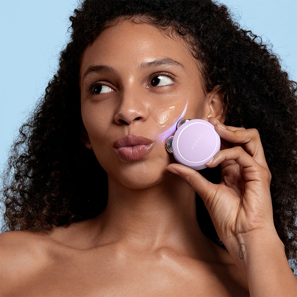 Femme avec un appareil facial violet sur le visage. Fond bleu. Elle sourit.