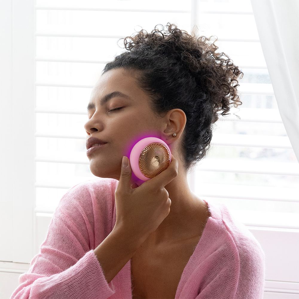Woman using a pink FOREO device on her face. Pink light is surrounding the device.