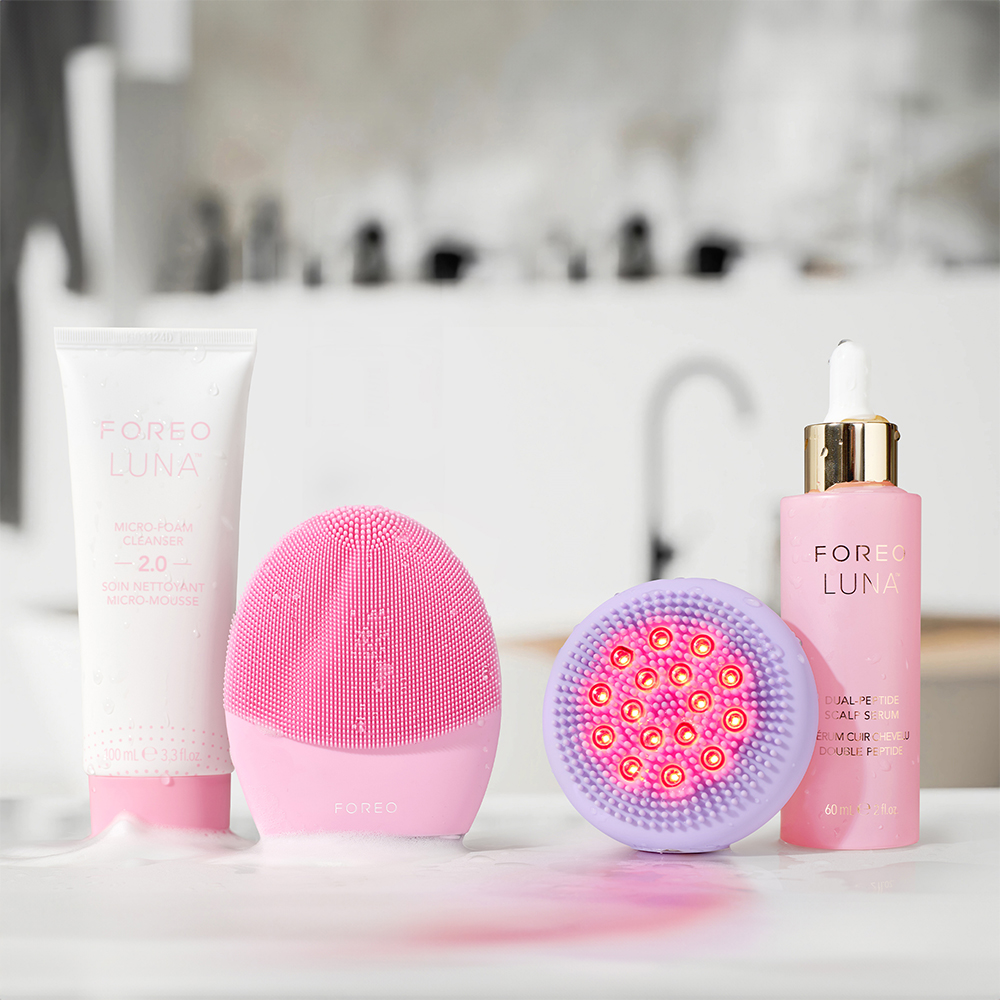 Foreo Luna-apparaten, reiniger en serum op een wit oppervlak, met een badkamerachtergrond.