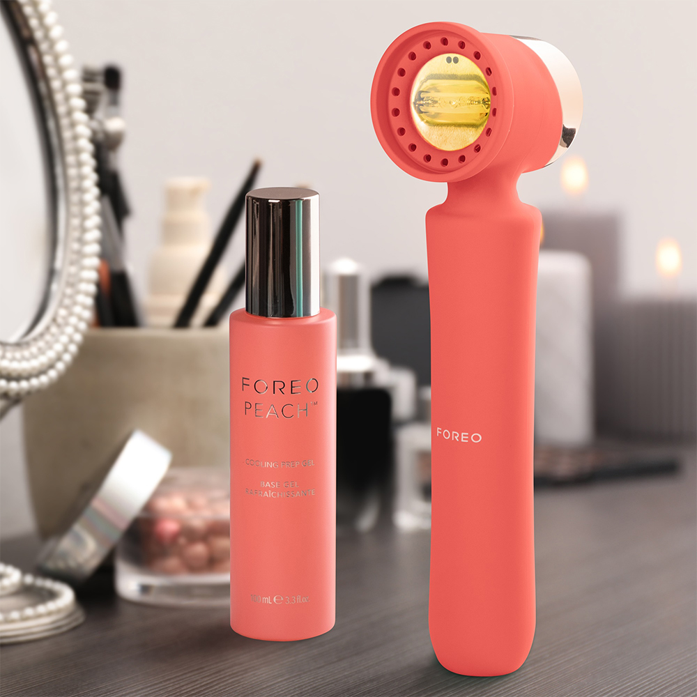 Peach-colored FOREO device and gel bottle sit on a vanity. The device has a round, red head with a handle.