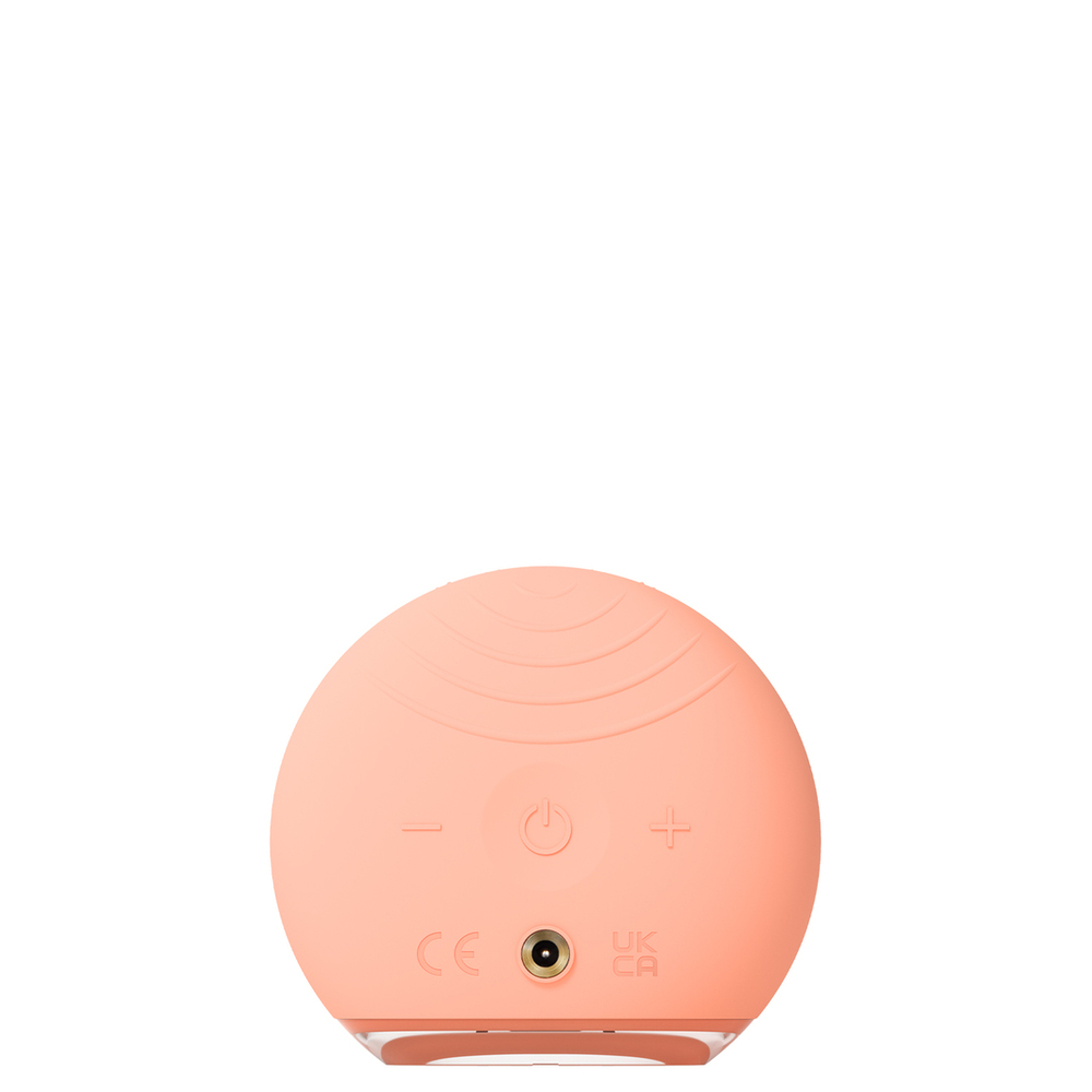 The back of a peach-colored FOREO device. Includes a power button, plus and minus buttons, and a charging port.