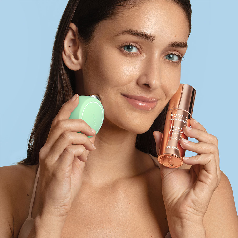 Woman with Foreo device and serum. She is smiling and holding the device and bottle.