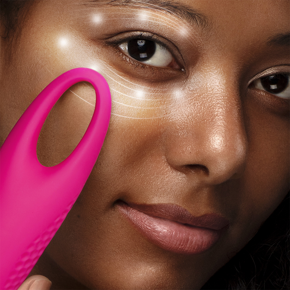 Visage de femme avec un appareil Foreo rose. Des lignes blanches mettent en valeur la peau. Foreo près de l'œil.