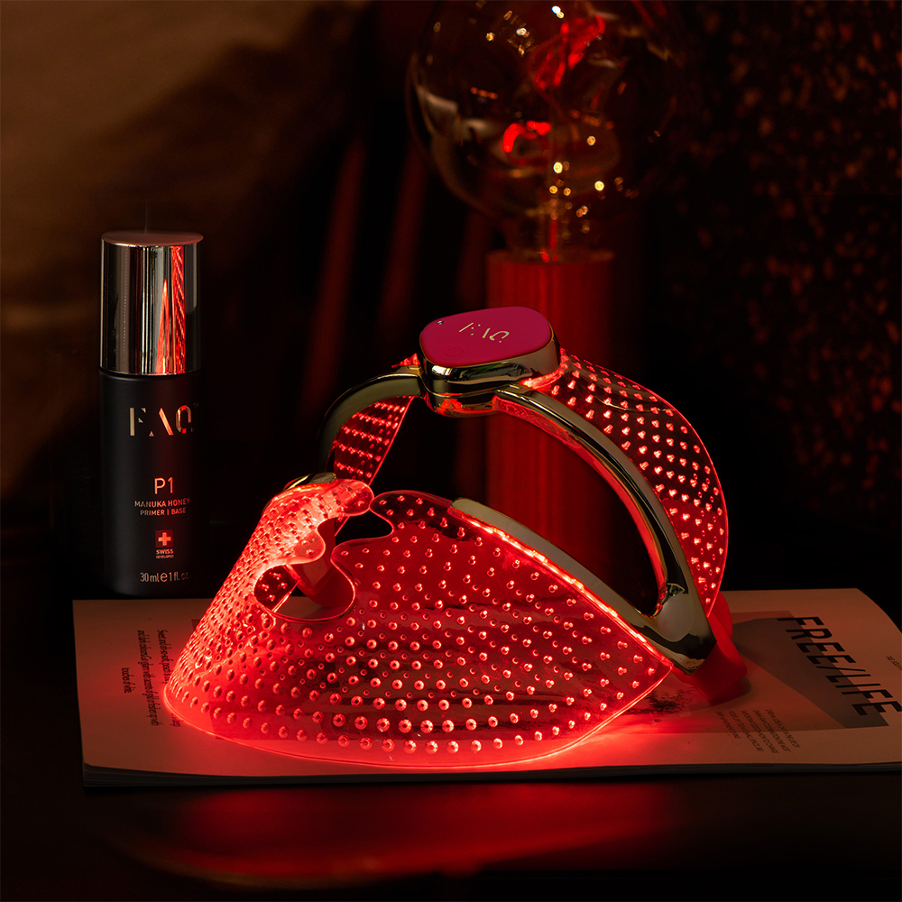 Appareil de beauté et masque facial à lumière rouge, une bouteille noire et un magazine sur une surface sombre.