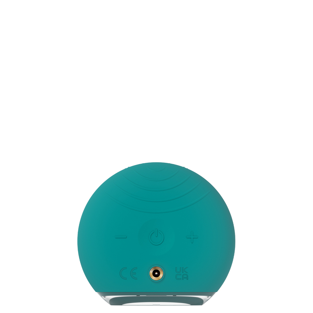 Teal green facial cleansing brush with control buttons on the back. The surface has a pattern of bumps.
