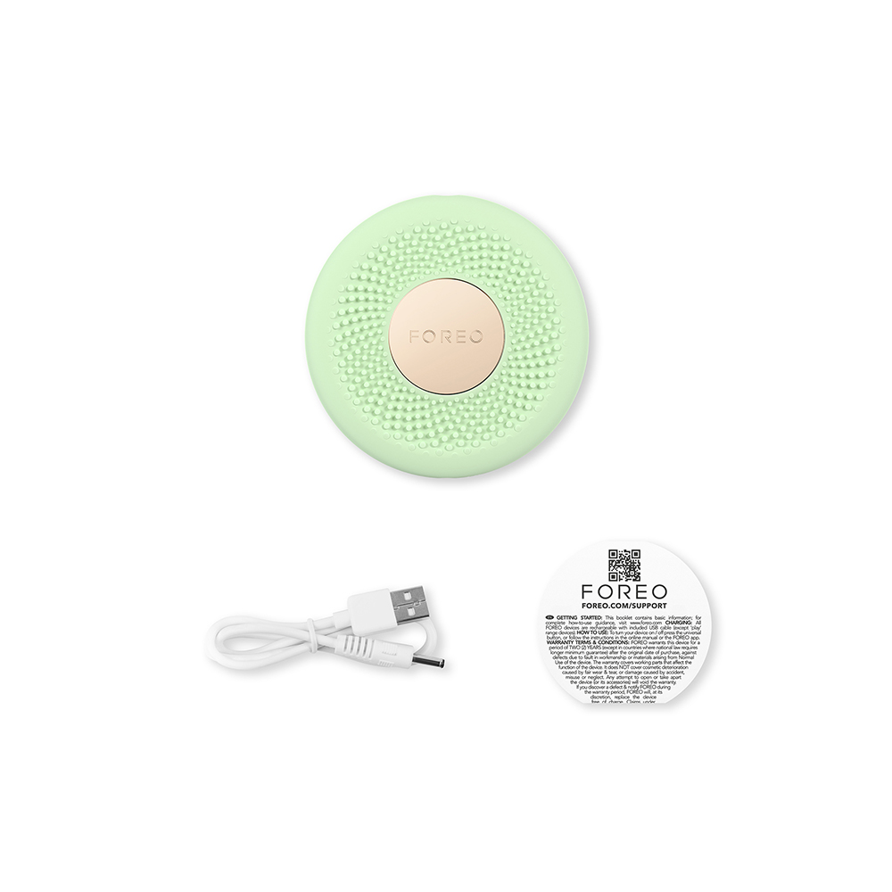 Mintgroen Foreo-apparaat met een kleine oplaadkabel en een Foreo-ondersteuningsgids op een witte achtergrond.