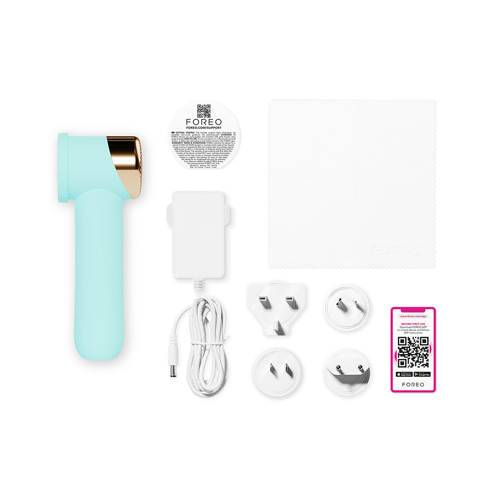 Teal facial device with charging accessories. White background.