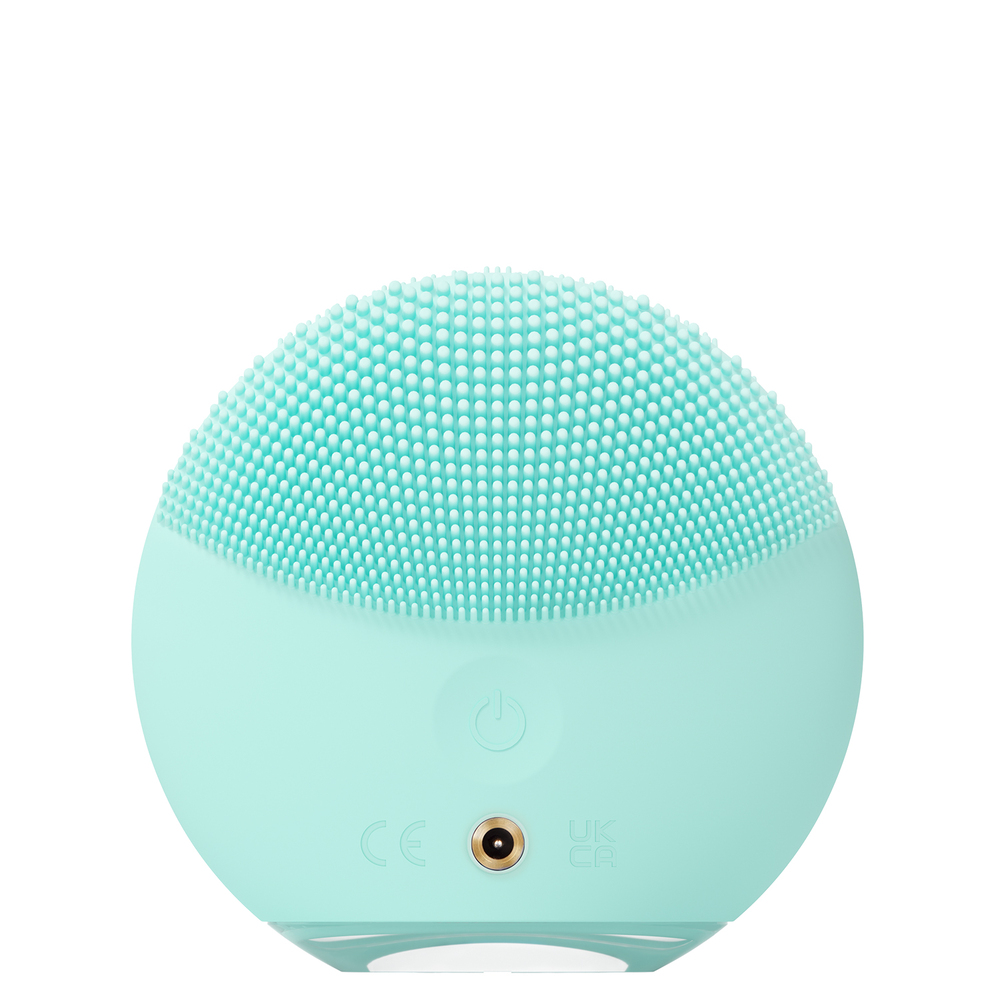 Close-up of a mint green facial cleansing device with a rounded head and button.