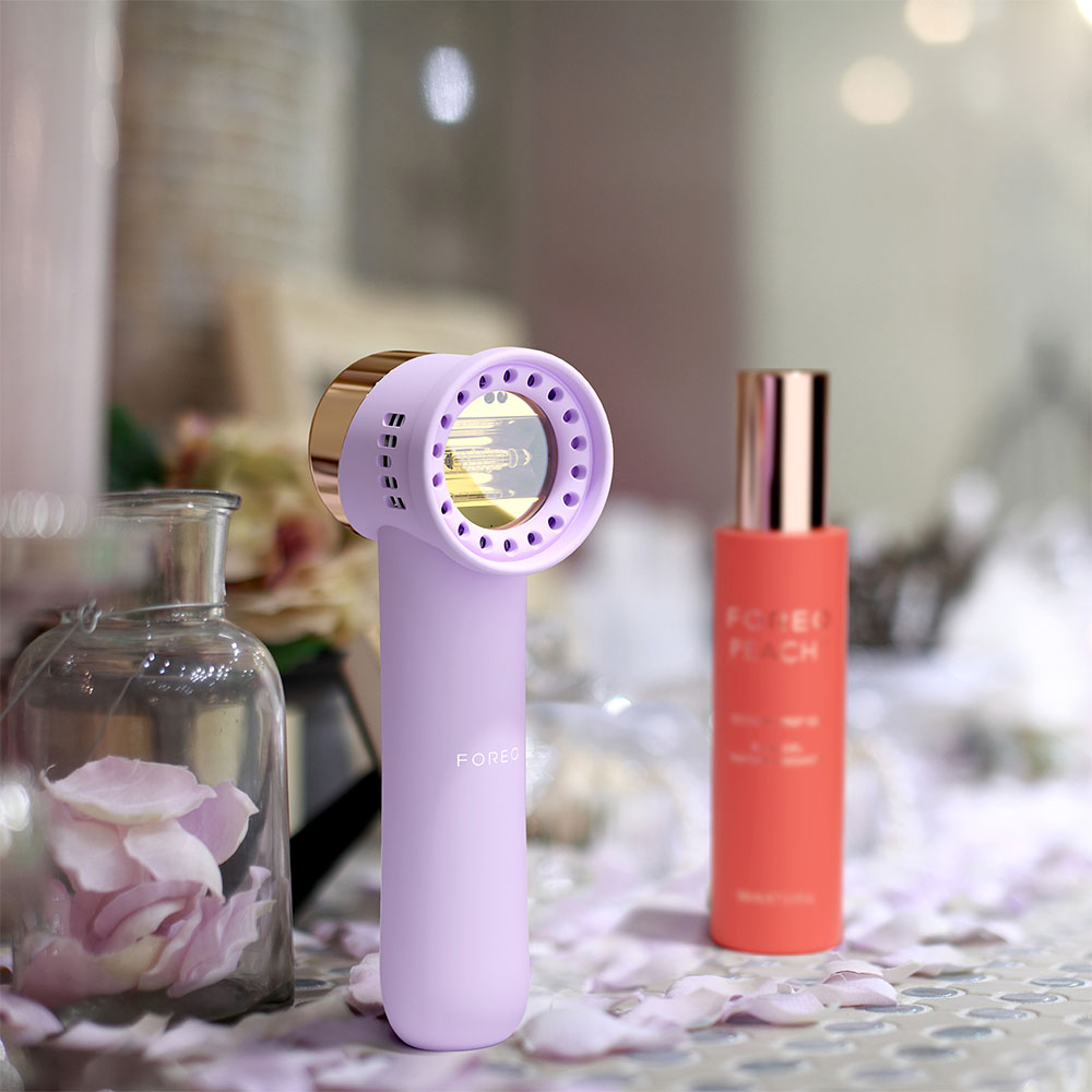Purple Foreo device and red Peach serum bottle with blurred background of a room setting.