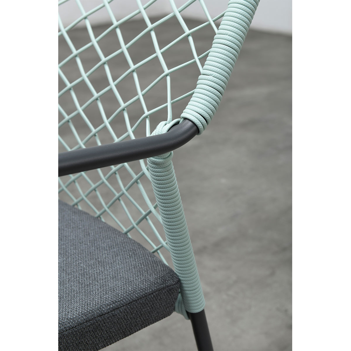 Close-up of a chair with a light green woven back and a grey cushion.