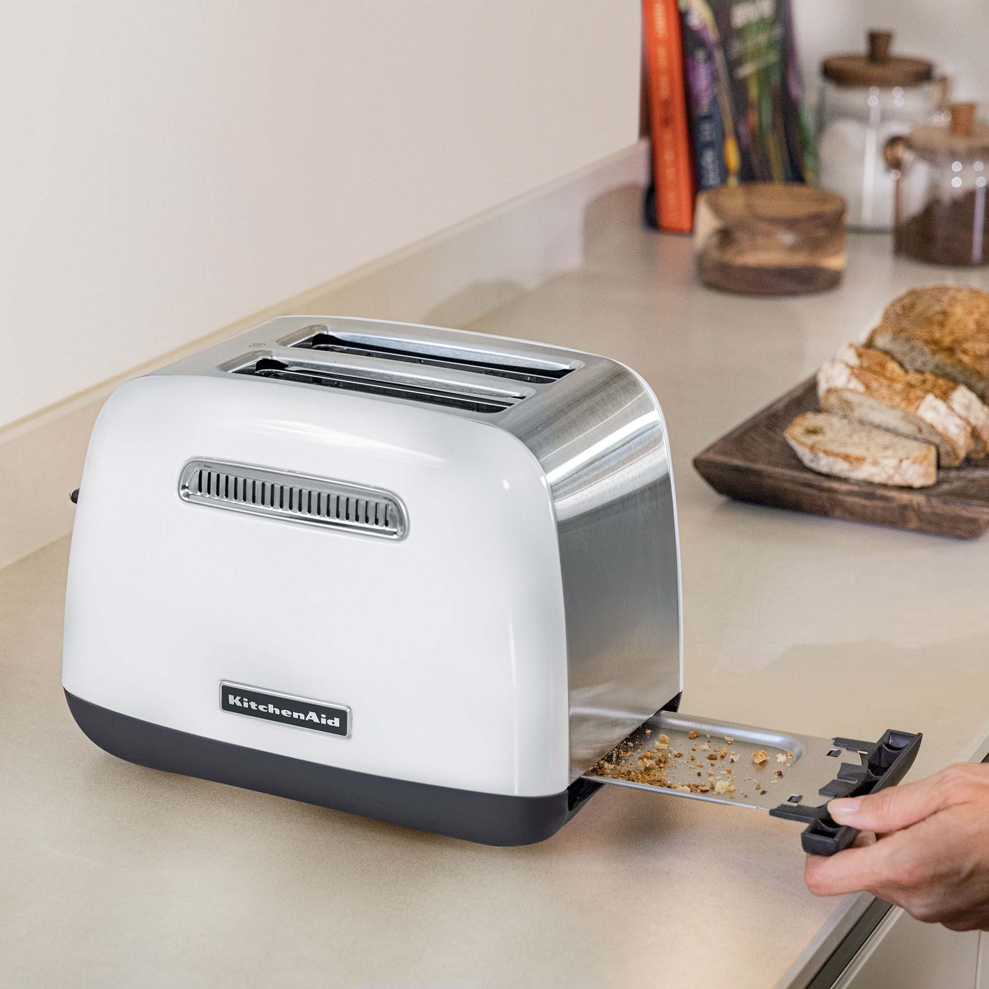 White KitchenAid toaster with crumb tray being pulled out, surrounded by ingredients.