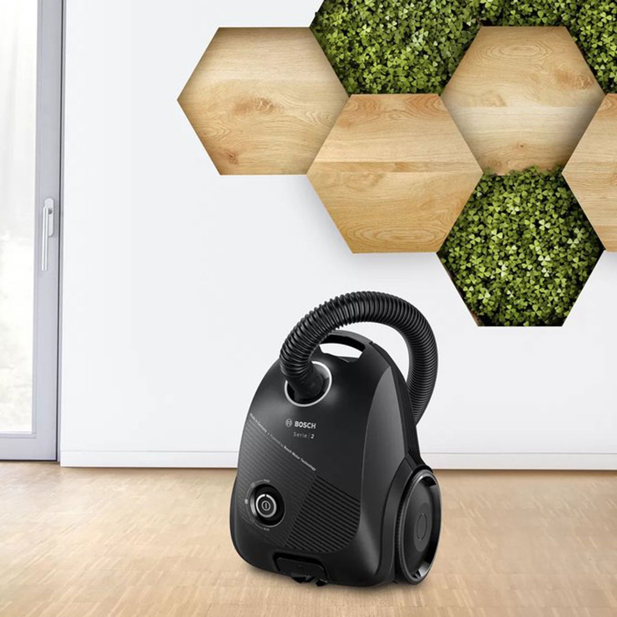 Czarny odkurzacz na drewnianej podłodze. Tło z dekoracją ścienną z drewna i roślin.
