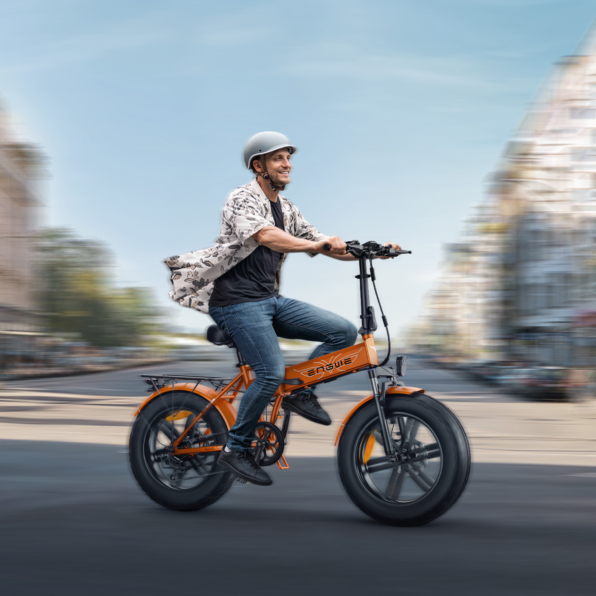 Hombre montando bicicleta eléctrica naranja en carretera, con casco y ropa informal, cielo azul.