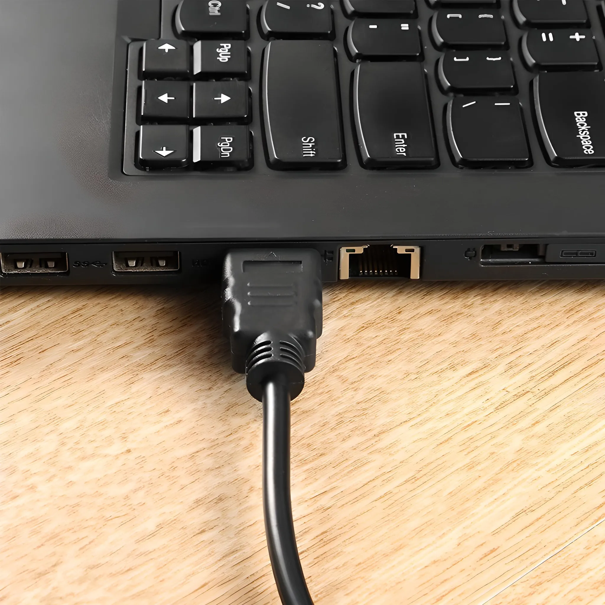 Laptop mit schwarzer Tastatur und schwarzem HDMI-Kabel. Holzoberfläche.