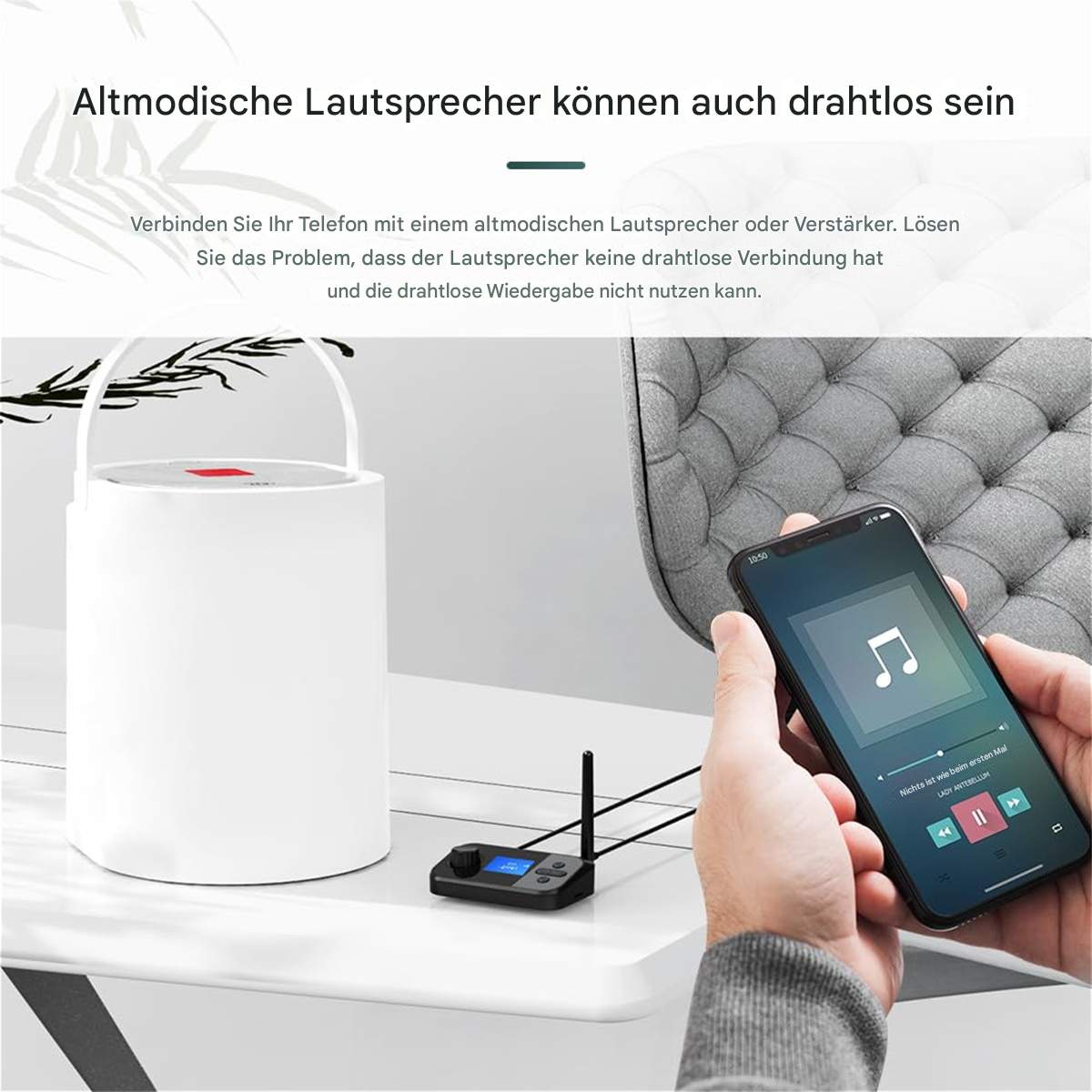 Eine Person hält ein Telefon, das mit einem weißen Audio-Transmitter mit Antenne verbunden ist. Der Hintergrund zeigt einen Lautsprecher.
