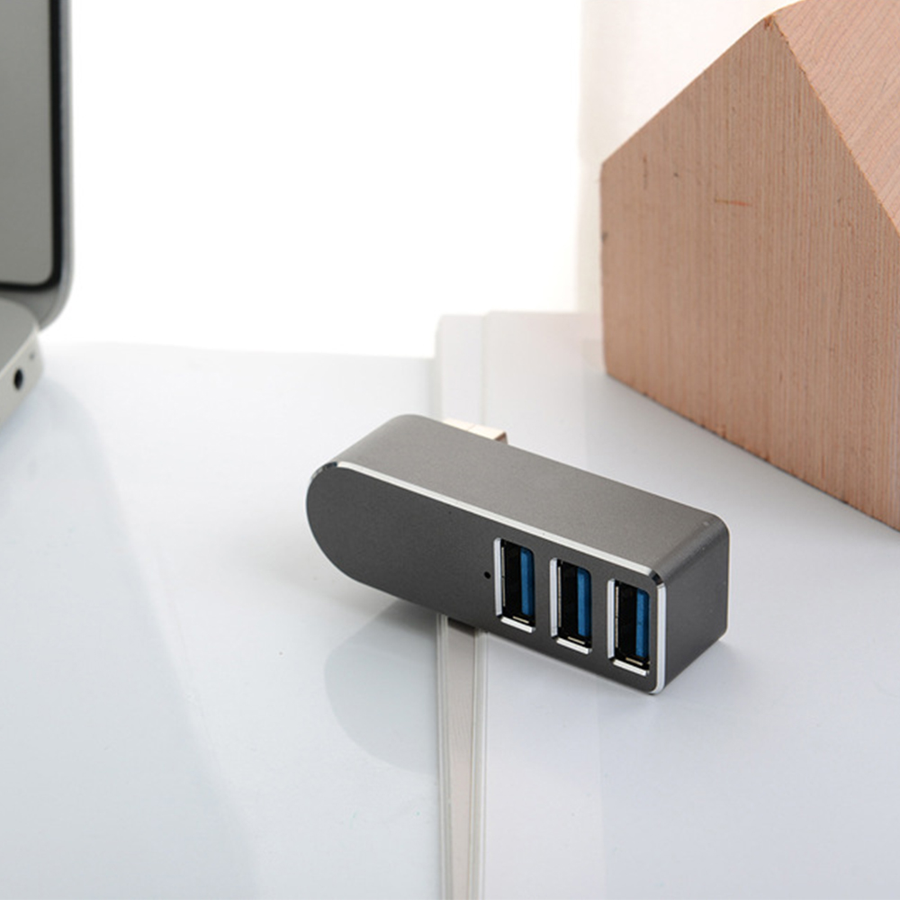 Ein silberner USB-Hub mit 3 blauen USB-Anschlüssen. Er liegt auf einer weißen Oberfläche mit einem Holzblock im Hintergrund.