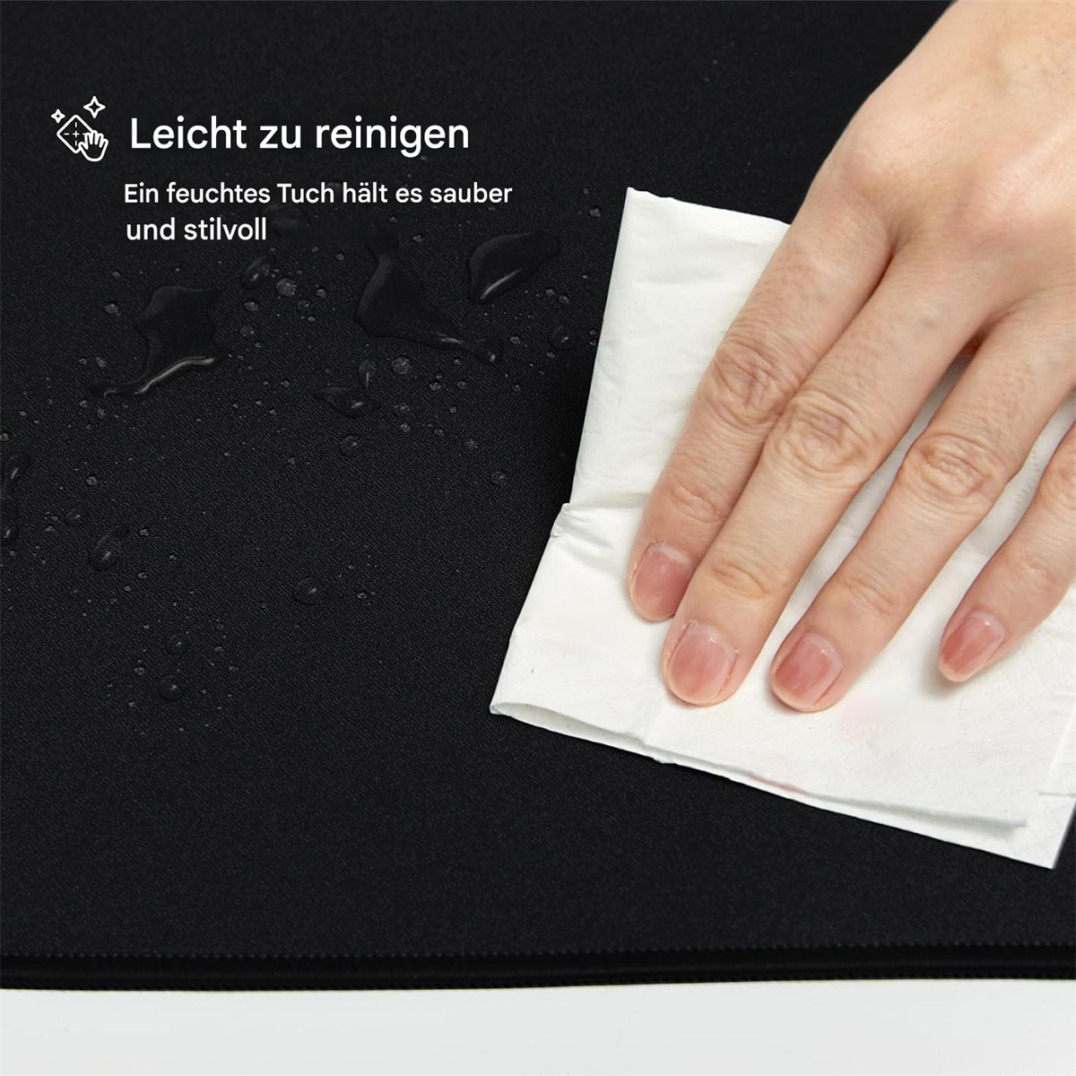 Eine Hand wischt eine schwarze Oberfläche mit einem weißen Tuch ab. Wassertropfen sind sichtbar.