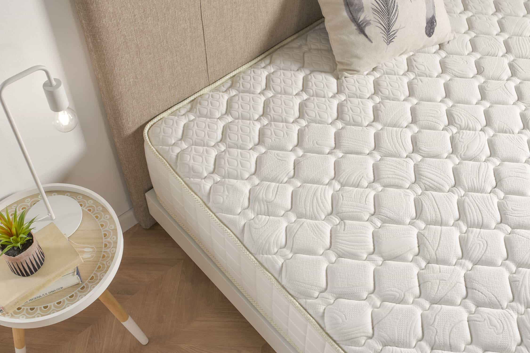 Cama con colchón estampado. Una almohada descansa en la cama. Lámpara y mesa cerca.