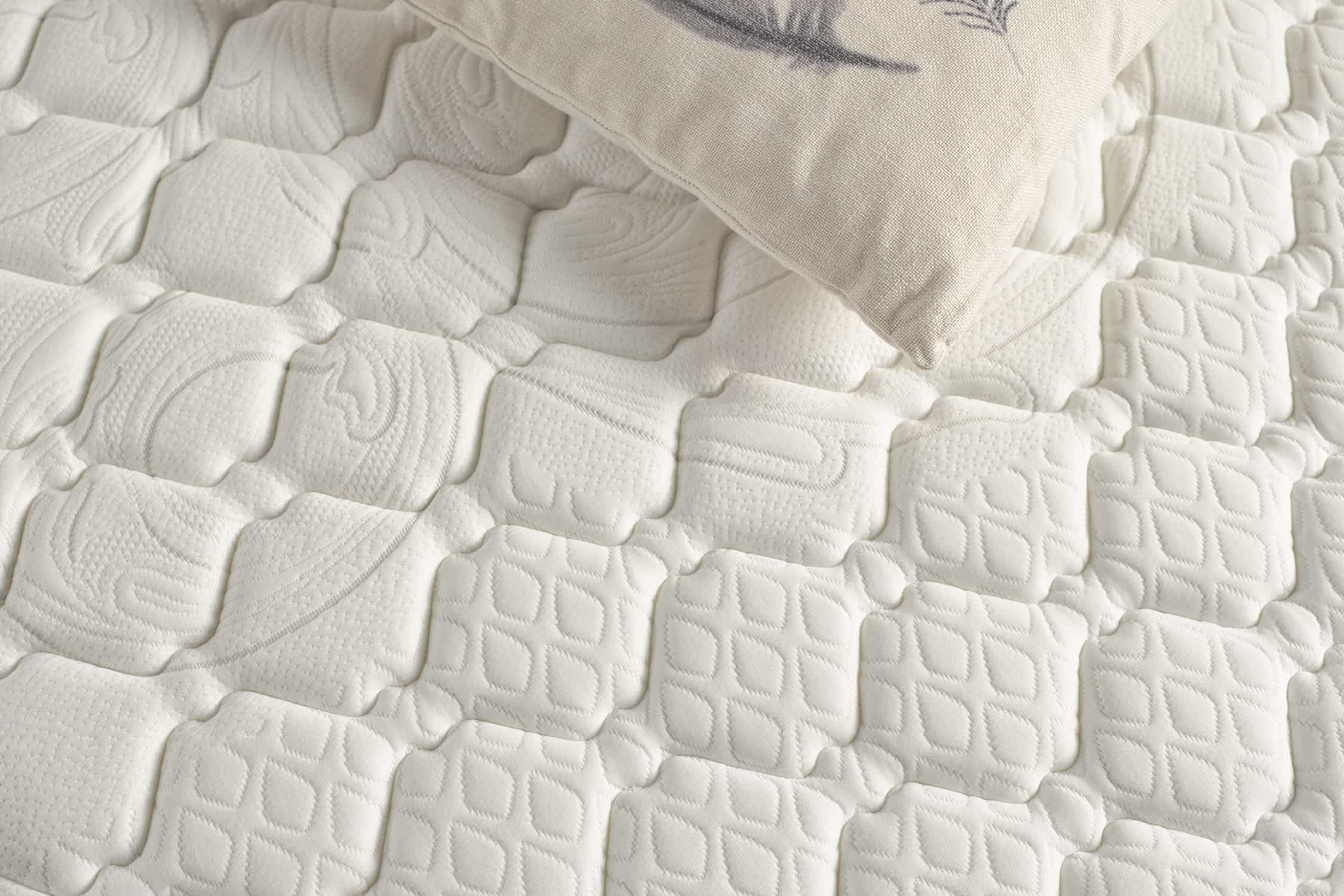 Primer plano de un colchón blanco acolchado, con una almohada decorativa encima.