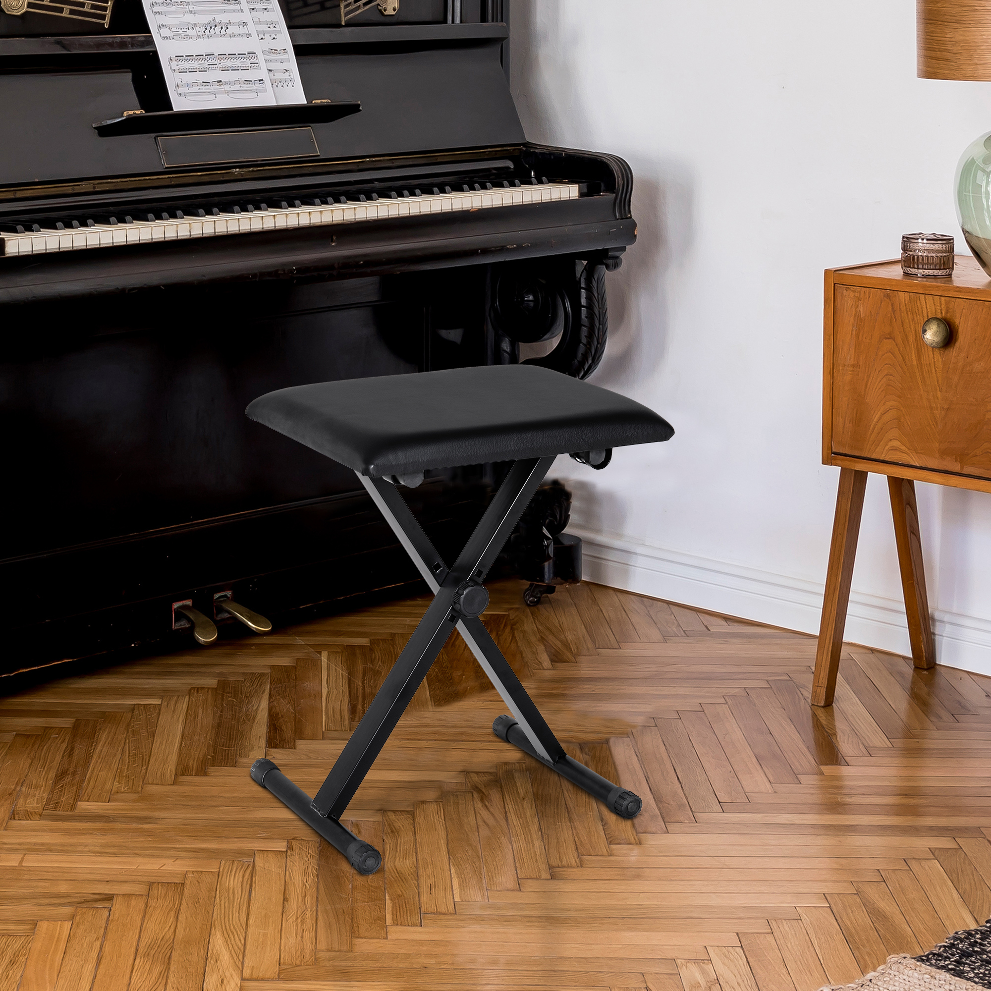 Ein schwarzer Klapphocker in einem Raum mit Klavier, Holzboden und Beistelltisch.