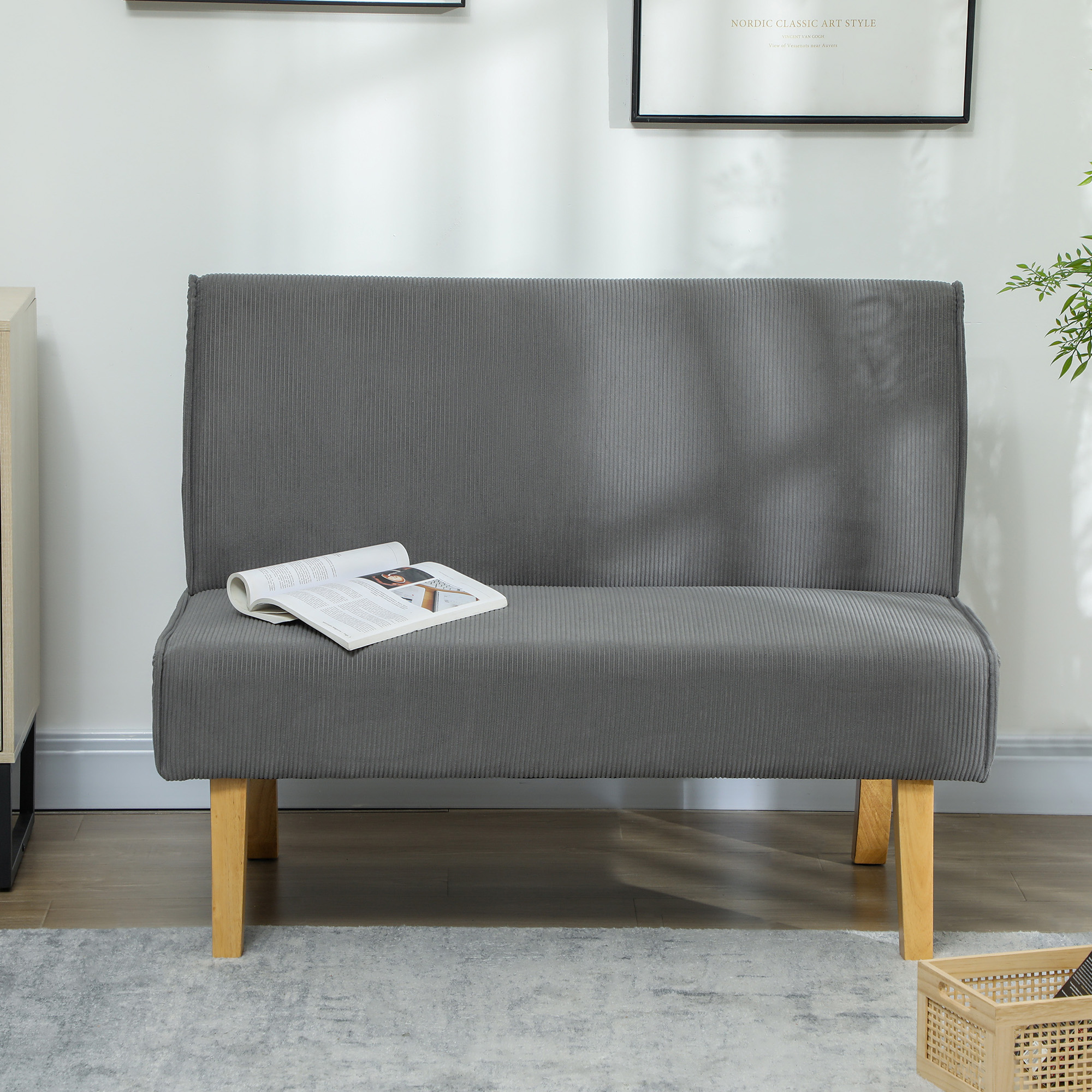 Ein graues Cordsofa, ein offenes Buch auf dem Sitz. Ein Korb und ein Poster an der Wand.