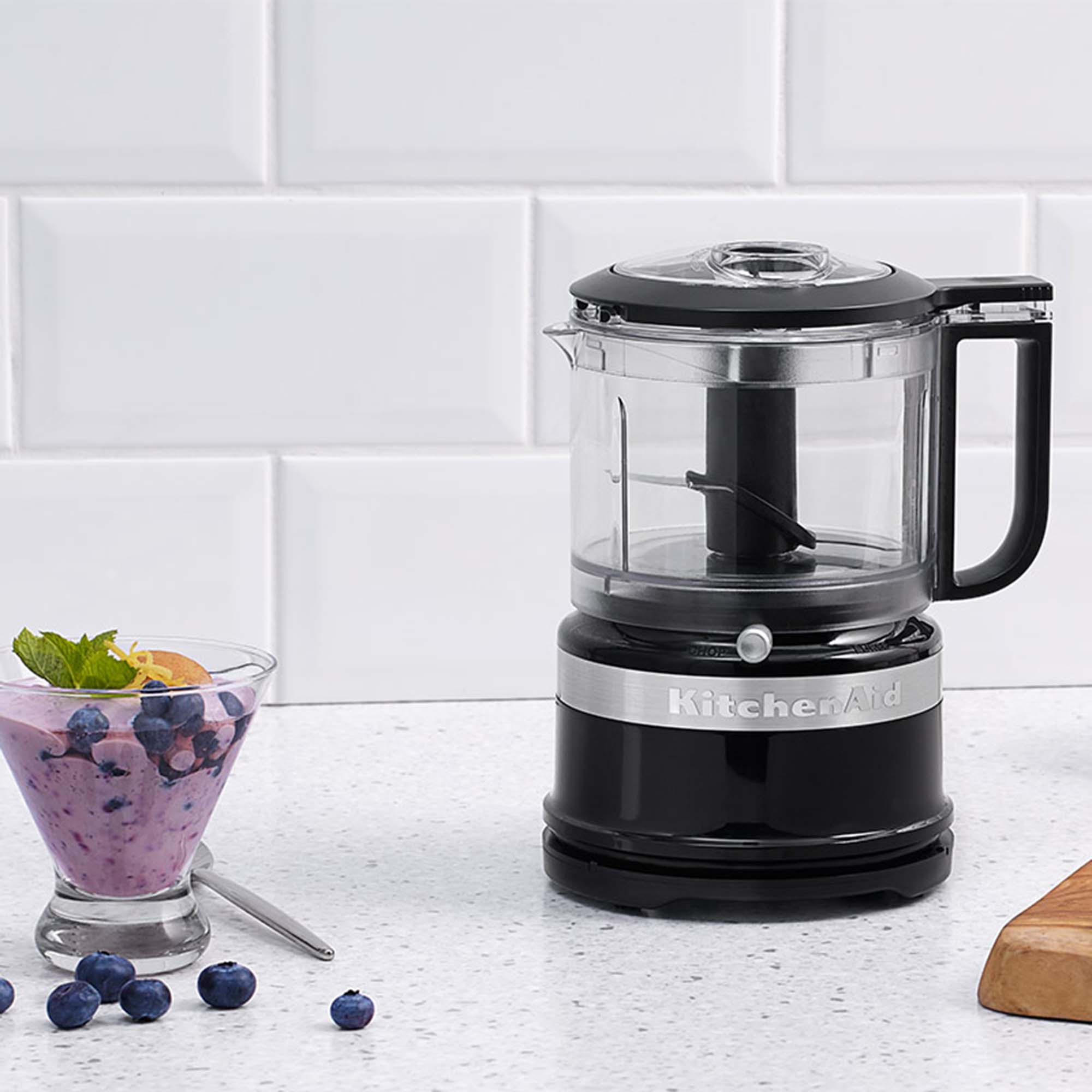 Siyah bir KitchenAid mutfak robotu, bir bardak yaban mersini smoothie'si ve yaban mersini yanında duruyor.
