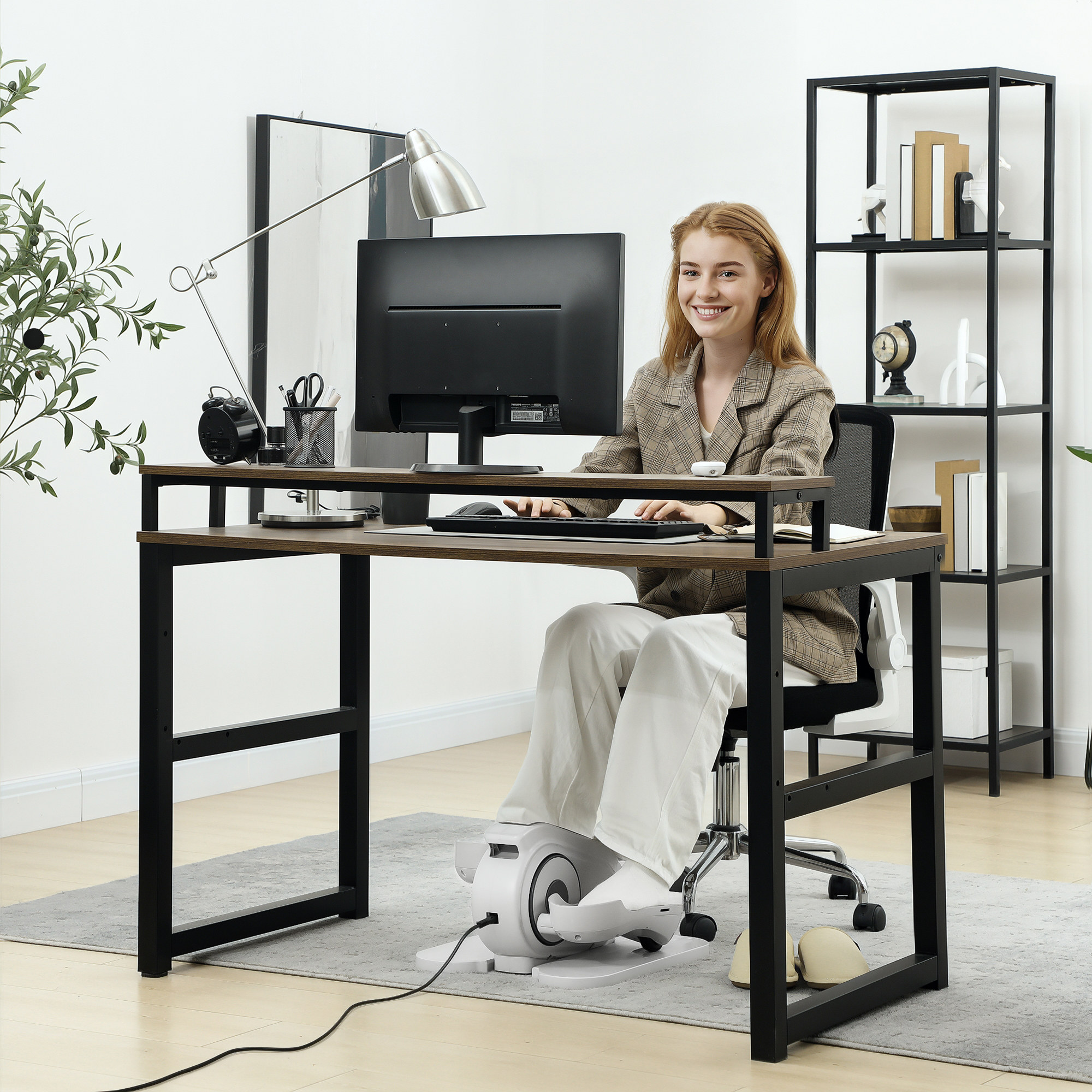 Frau arbeitet an einem Schreibtisch mit Computer und Ellipsentrainer unter dem Tisch.