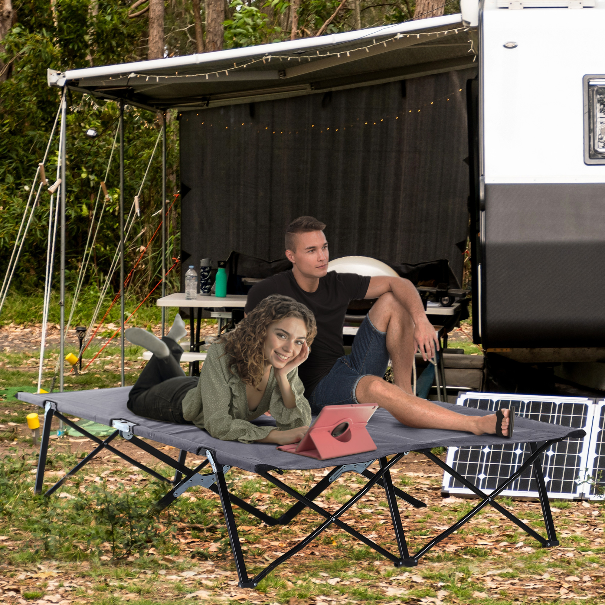 Ein Paar liegt auf einem grauen Klappbett in einem Camp mit Anhänger und Solarpanels.
