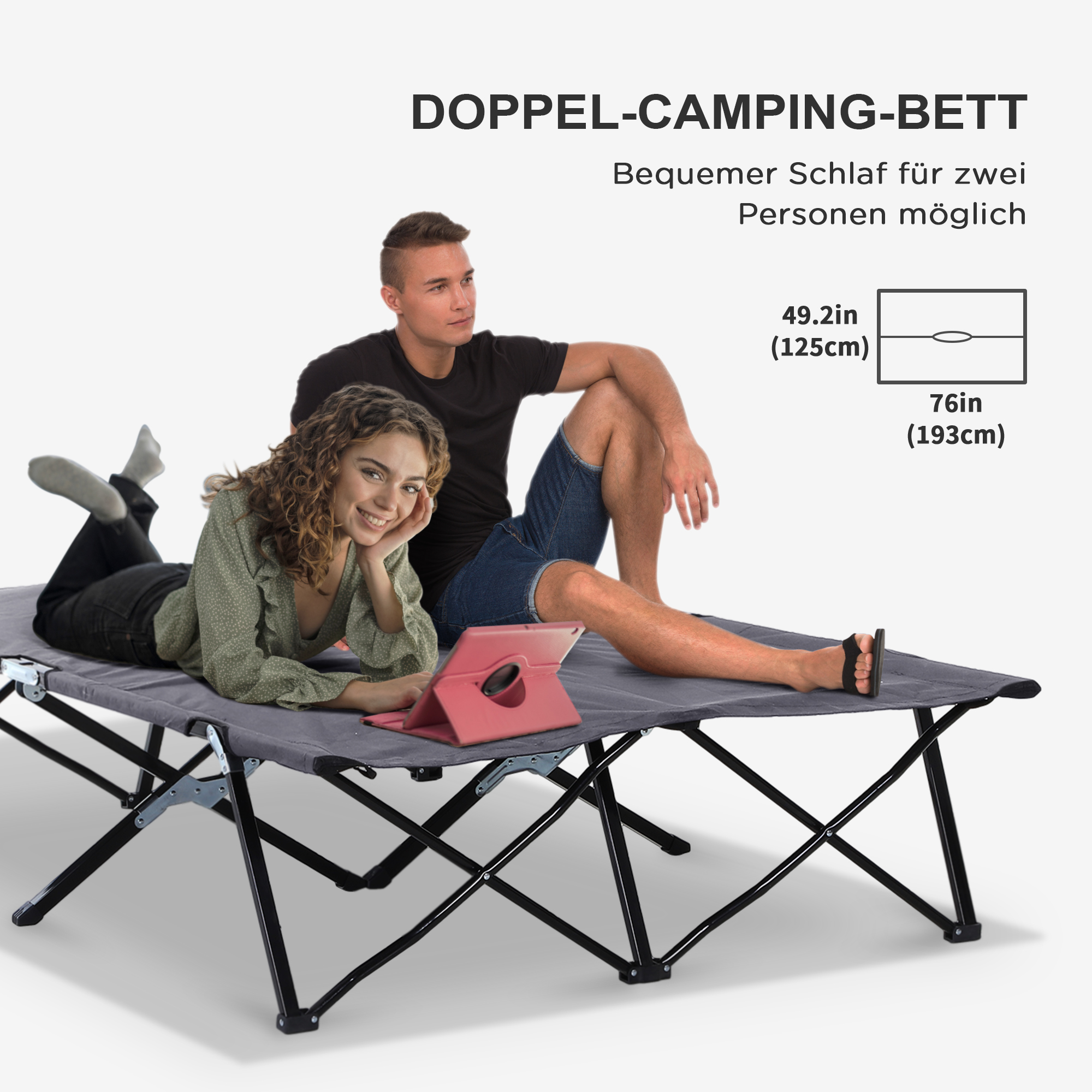 Paar sitzt auf einem grauen Campingbett. Sie lächeln und benutzen ein Tablet.