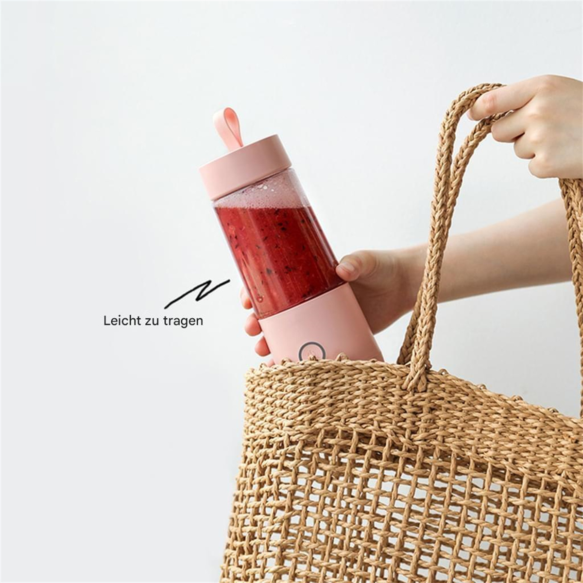 Ein pinkfarbener tragbarer Mixer in einer Strohtasche, mit roter Flüssigkeit darin.