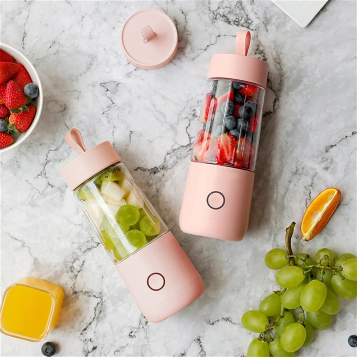 Zwei pinkfarbene tragbare Mixer mit Früchten und andere Früchte wie Trauben und Erdbeeren.