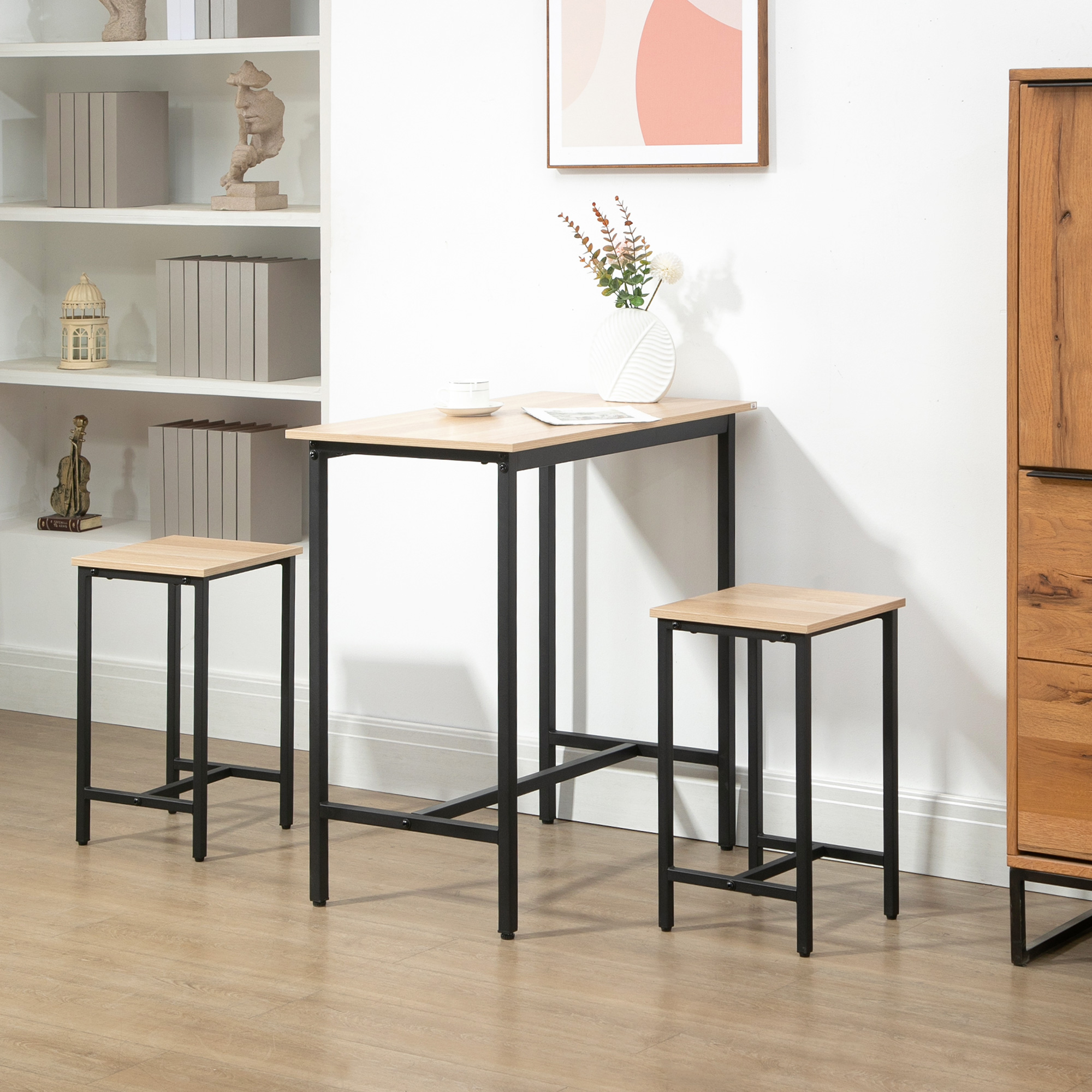 Ein kleiner Tisch und zwei Hocker mit hellen Holzplatten und schwarzen Rahmen vor einer weißen Wand.
