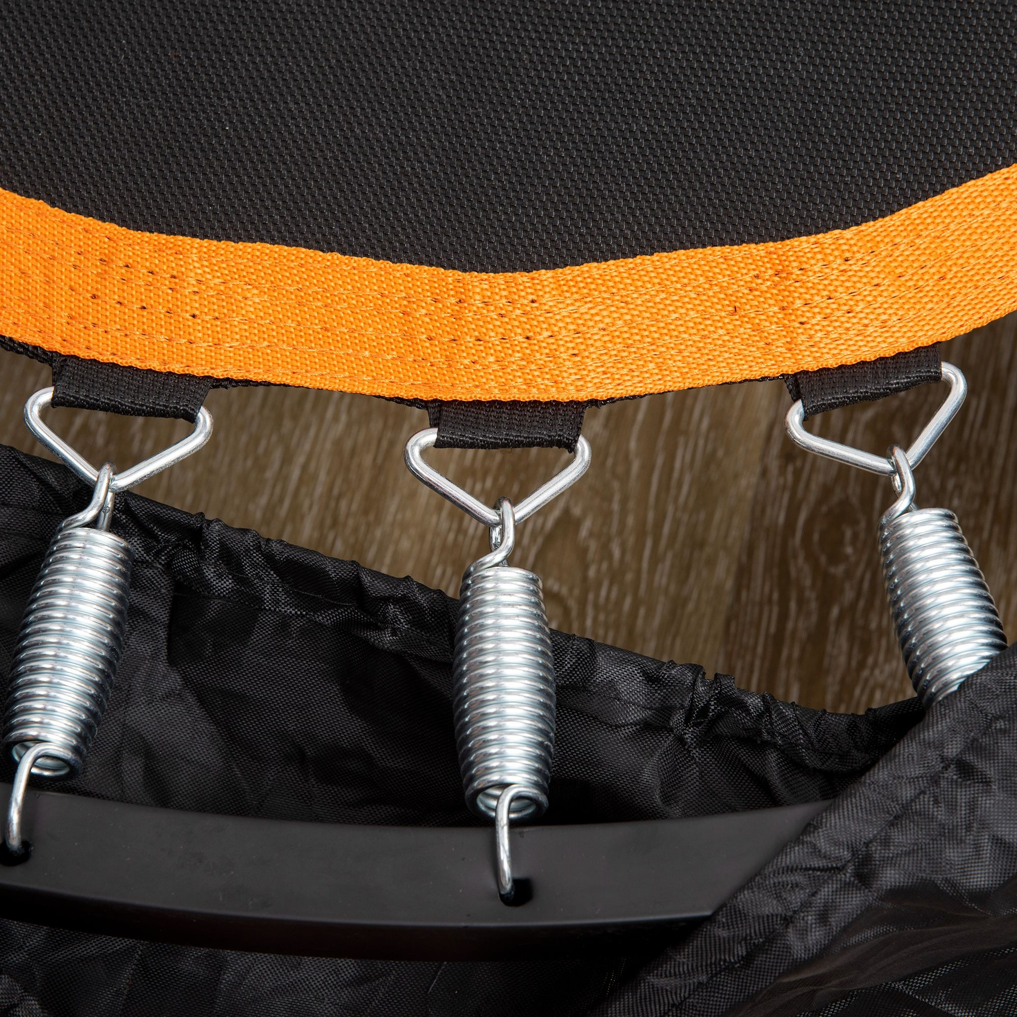 Nahaufnahme der Federn, die das schwarze Trampolin mit dem orangefarbenen Rand verbinden.