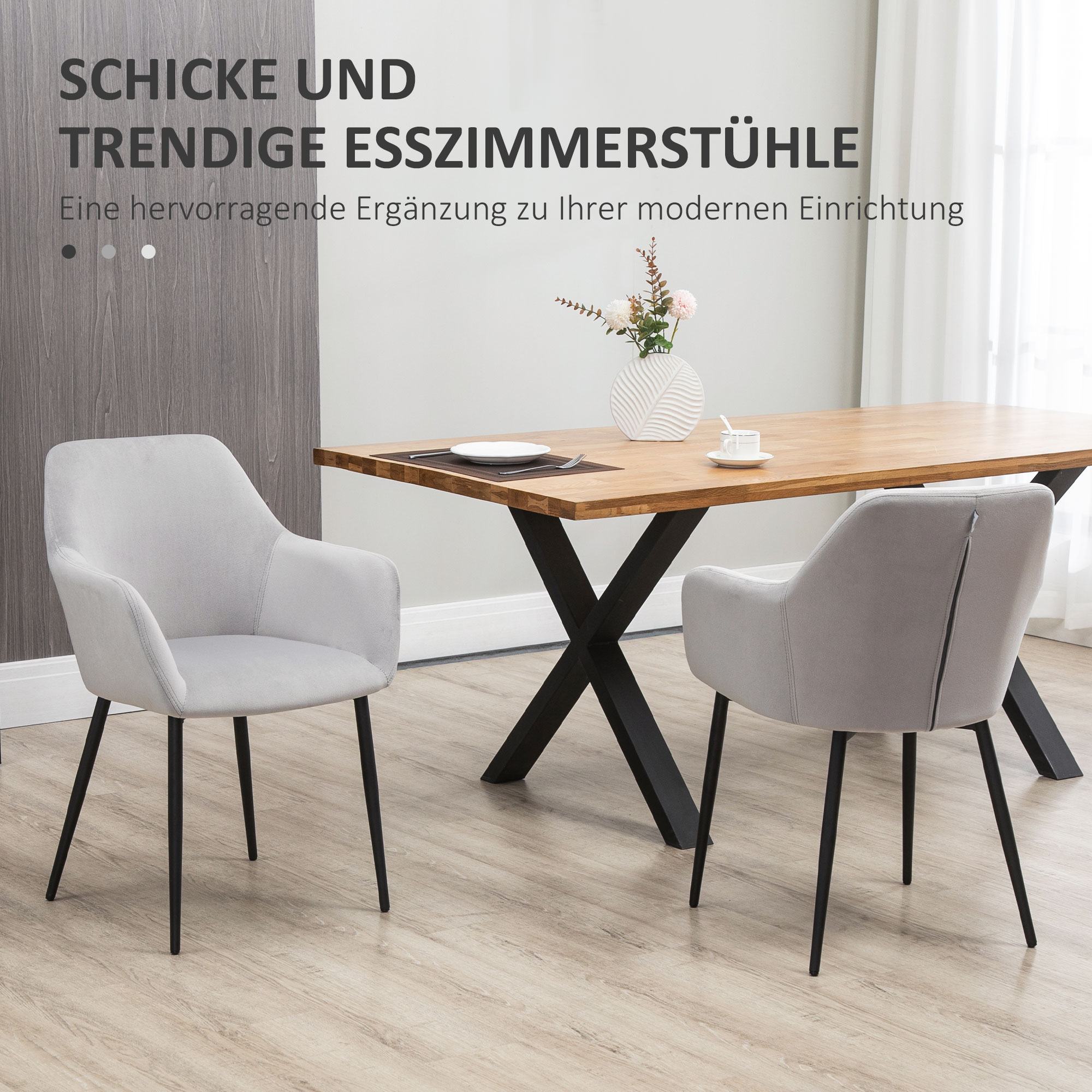 Zwei graue Stühle mit schwarzen Beinen neben einem Holztisch. Weiße Vase mit Blumen auf dem Tisch.