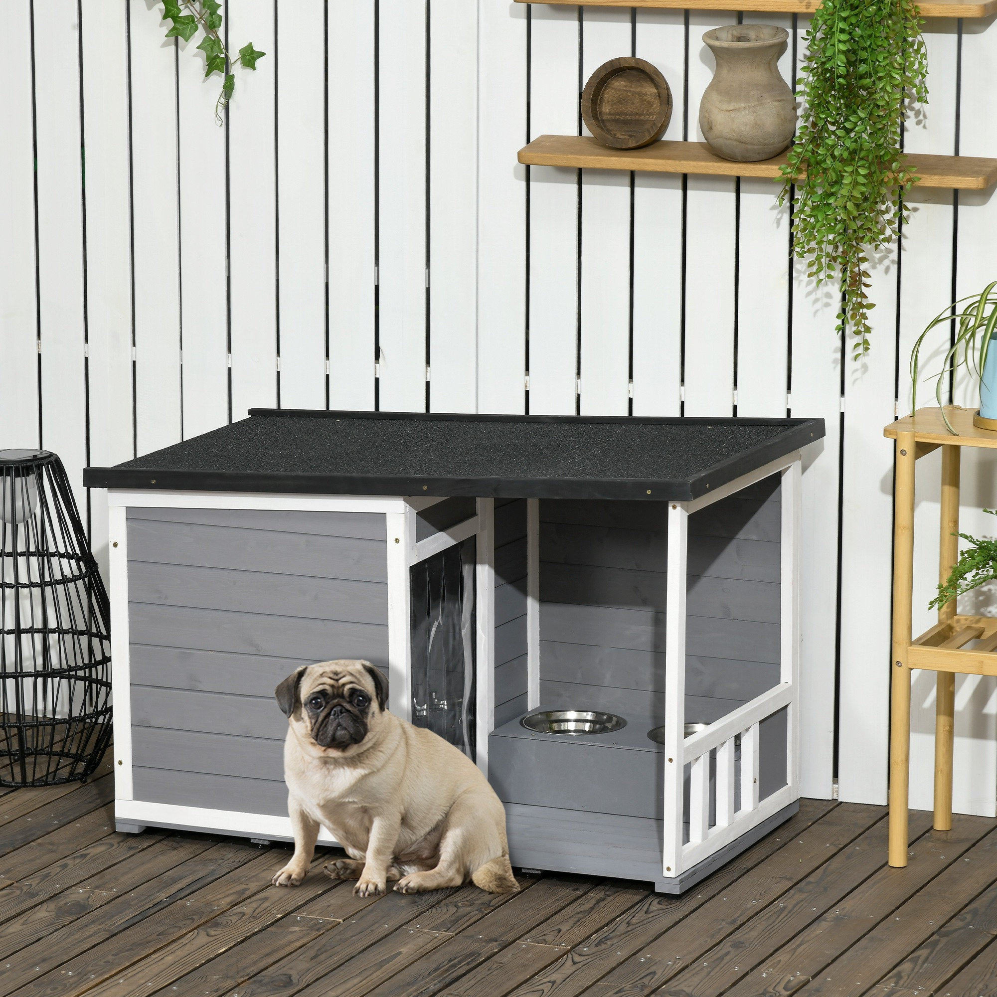 Eine Möpse sitzt vor einem grauen Hundehäuschen. Das Haus steht auf einer Holzterrasse.