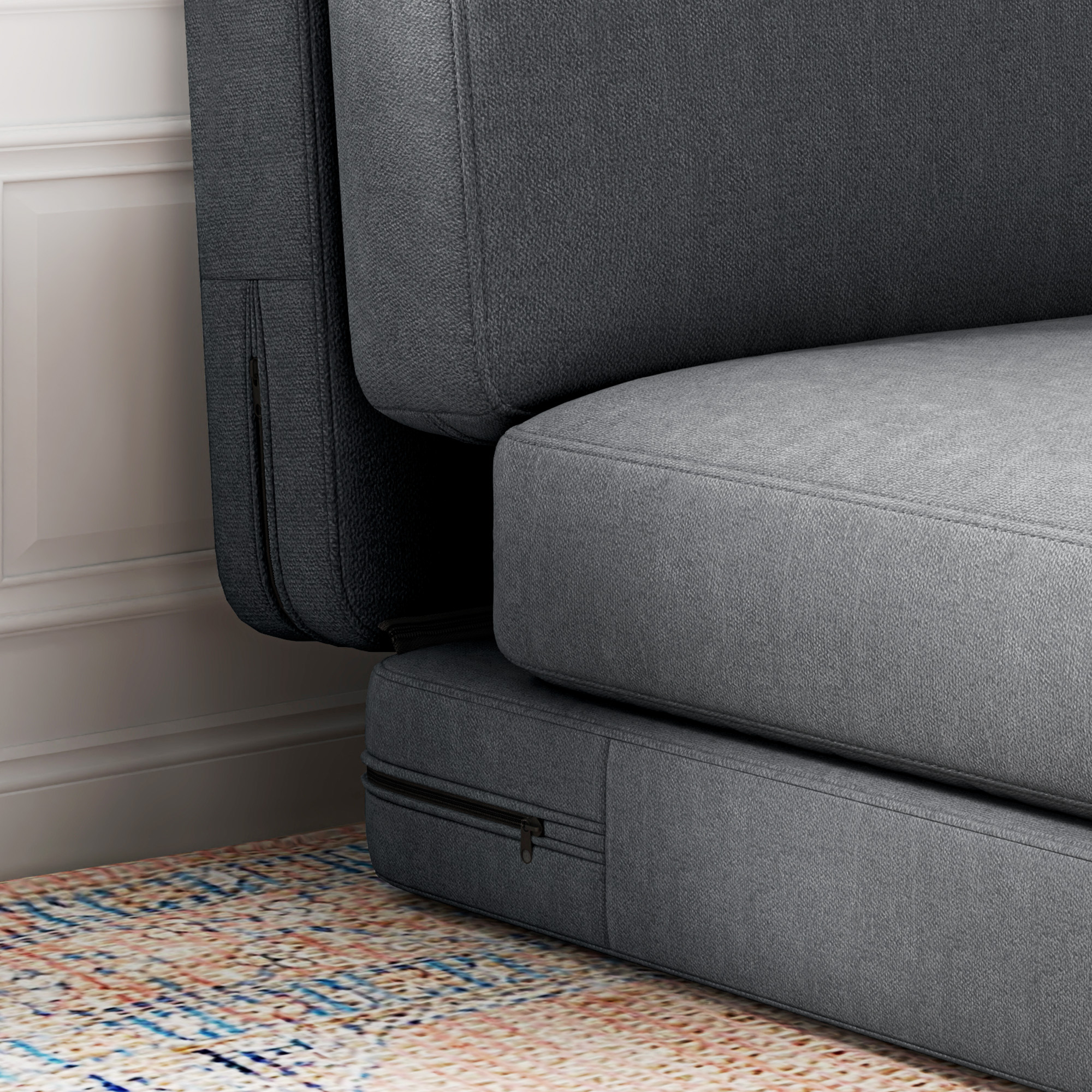 Nahaufnahme eines grauen Sofas mit sichtbaren Nähten und einem Reißverschluss. Der Hintergrund hat einen gemusterten Teppich.