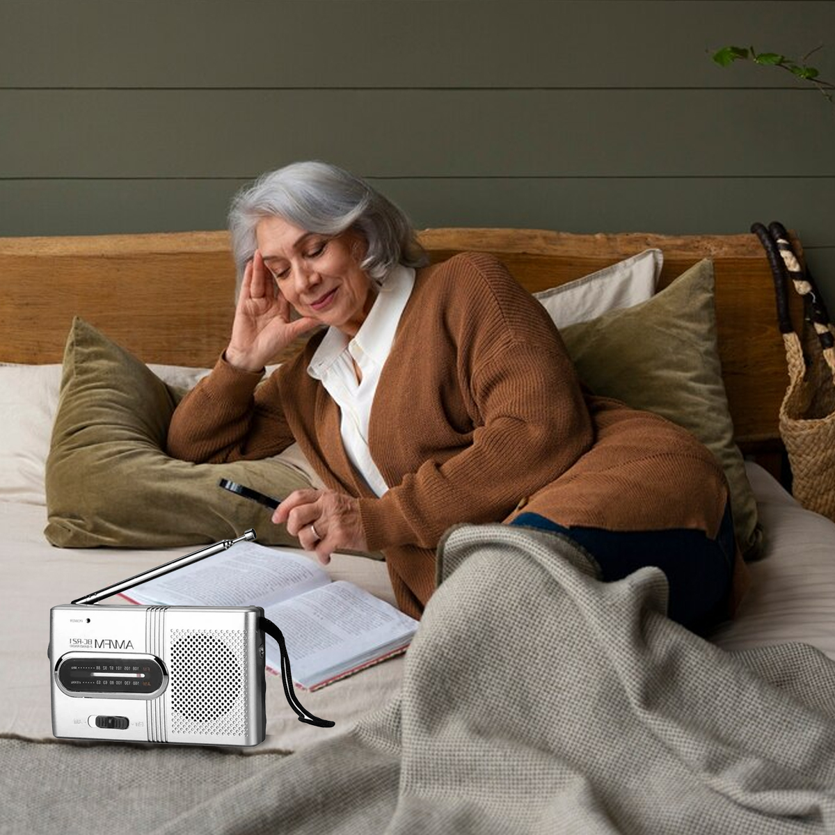 Ältere Frau liest im Bett mit einem Radio. Sie benutzt eine Lupe.